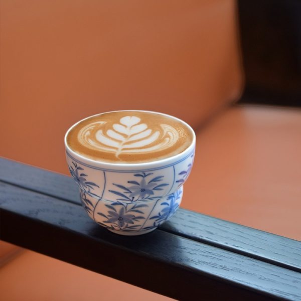 Blue and white ceramic cup filled with coffee on wooden rack, showcasing Chinese style