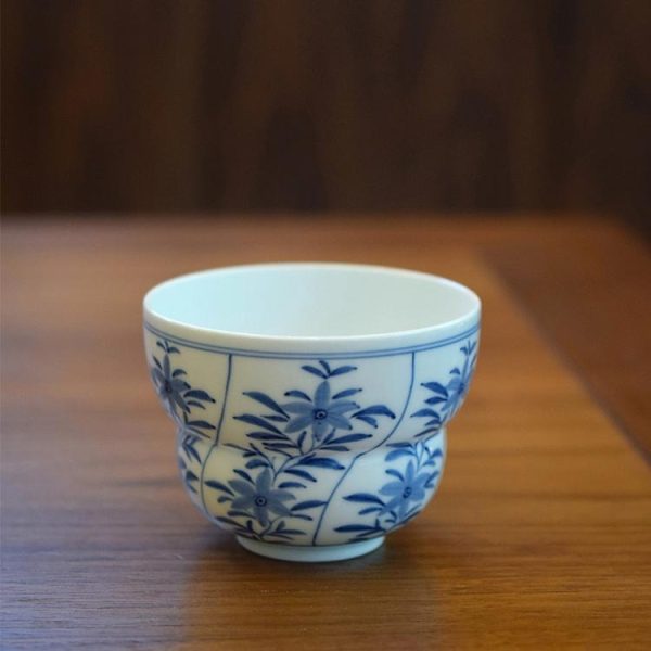 Blue and white porcelain gourd cup with hand-painted six-petal floral design on brown wooden table