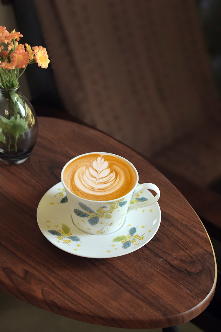 A bouquet of flowers and a cup of rich Jamaica Blue Mountain coffee in the Osmanthus Rabbit Ceramic Coffee Cup, set on a wooden table creating a serene and elegant living scene