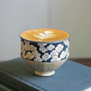 Hand-painted underglaze ceramic cup with cloud pattern, thick and elegant design, placed on a book.