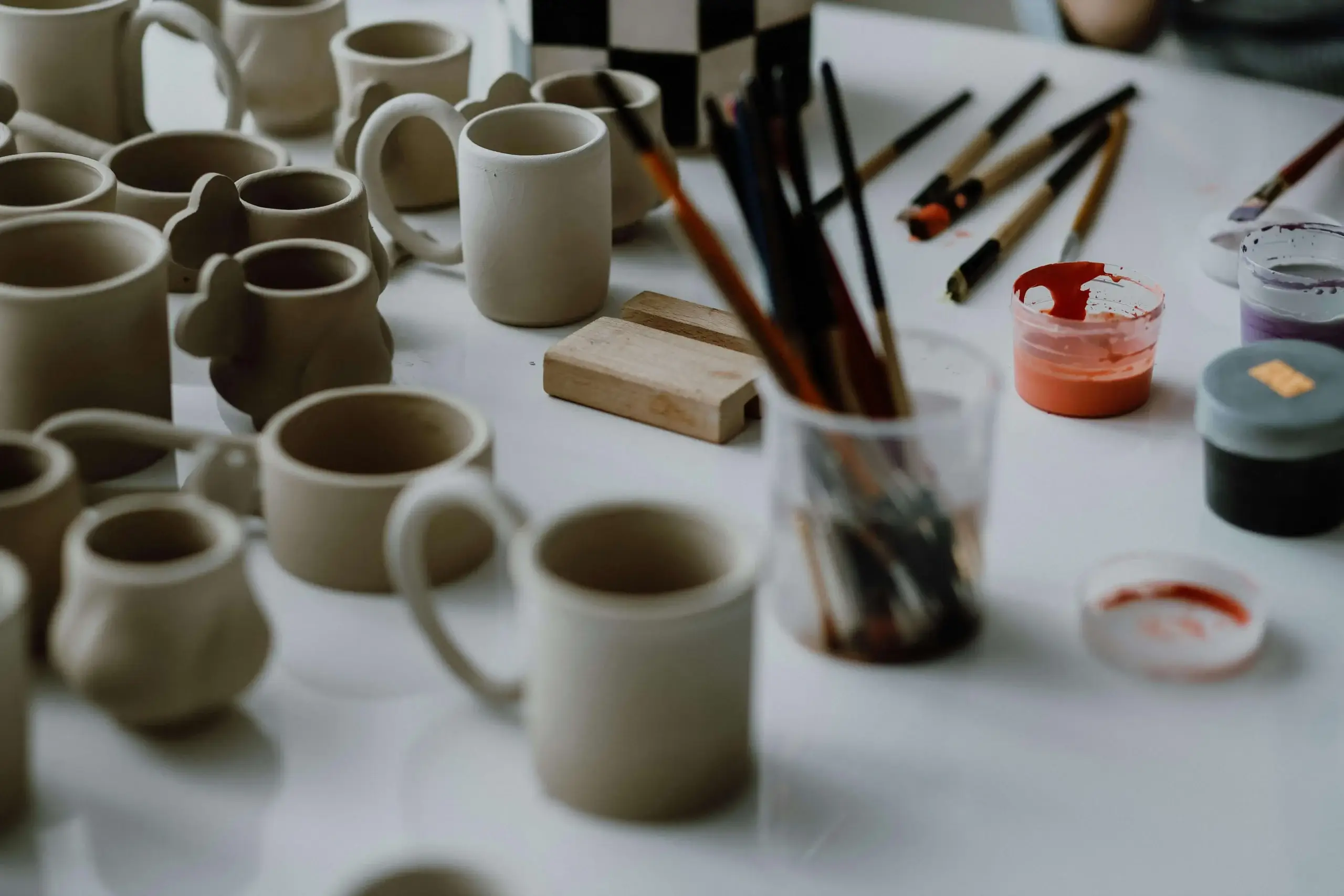 Handmade ceramic cups and painting tools in an artisan's studio.
