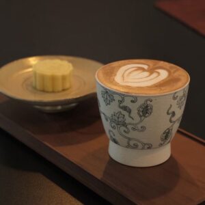 Chinese-style ceramic coffee cup with latte and dessert in a café setting.