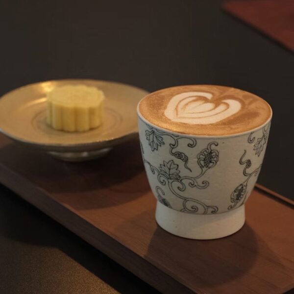 Chinese-style ceramic coffee cup with latte and dessert in a café setting.