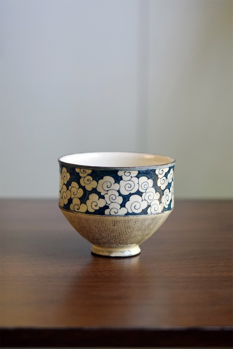 Hand-painted ceramic coffee cup with cloud motif in under-glaze style on table, showcasing traditional Chinese Primitive elegance aesthetics
