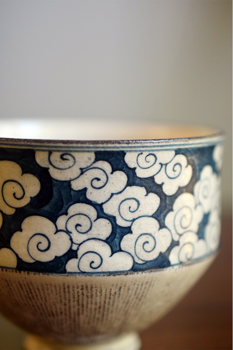 Detail of hand-crafted ceramic coffee cup with cloud motif in blue-and-white underglaze, showing refined painted lines
