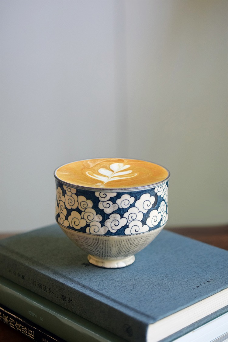 Underglaze cloud-pattern ceramic cup with clear hand-painted design, filled with coffee, showing smooth texture