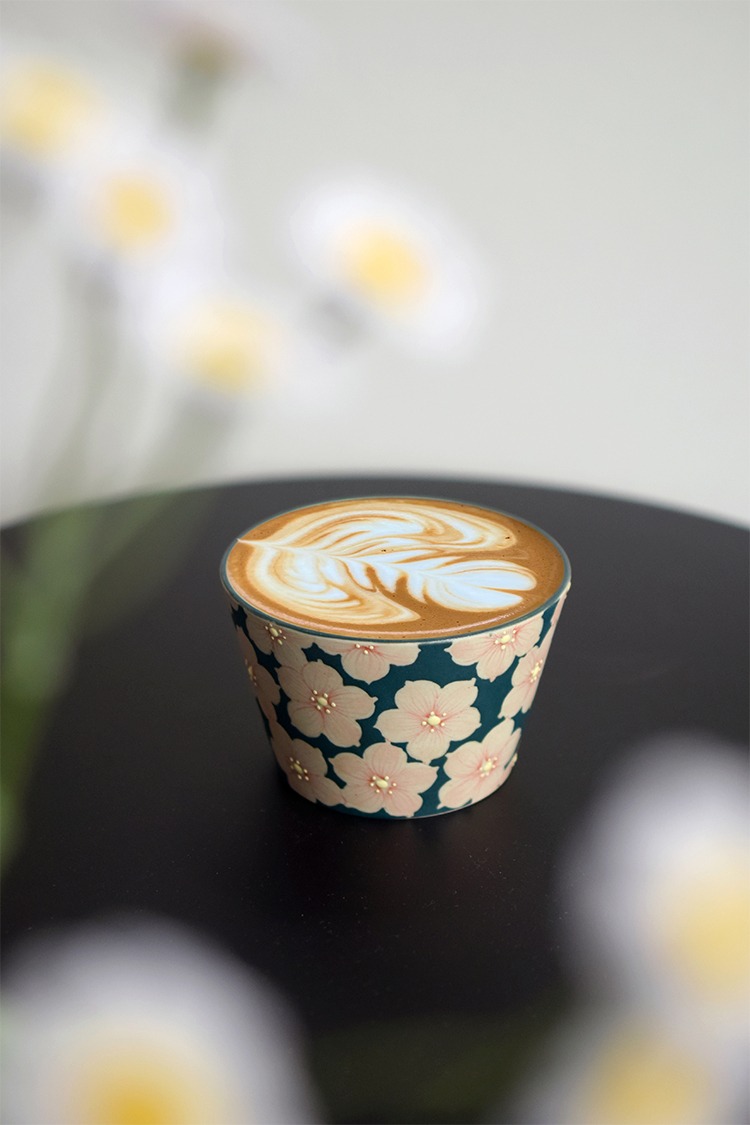 Handmade cherry blossom ceramic latte cup sitting elegantly on an office desk.