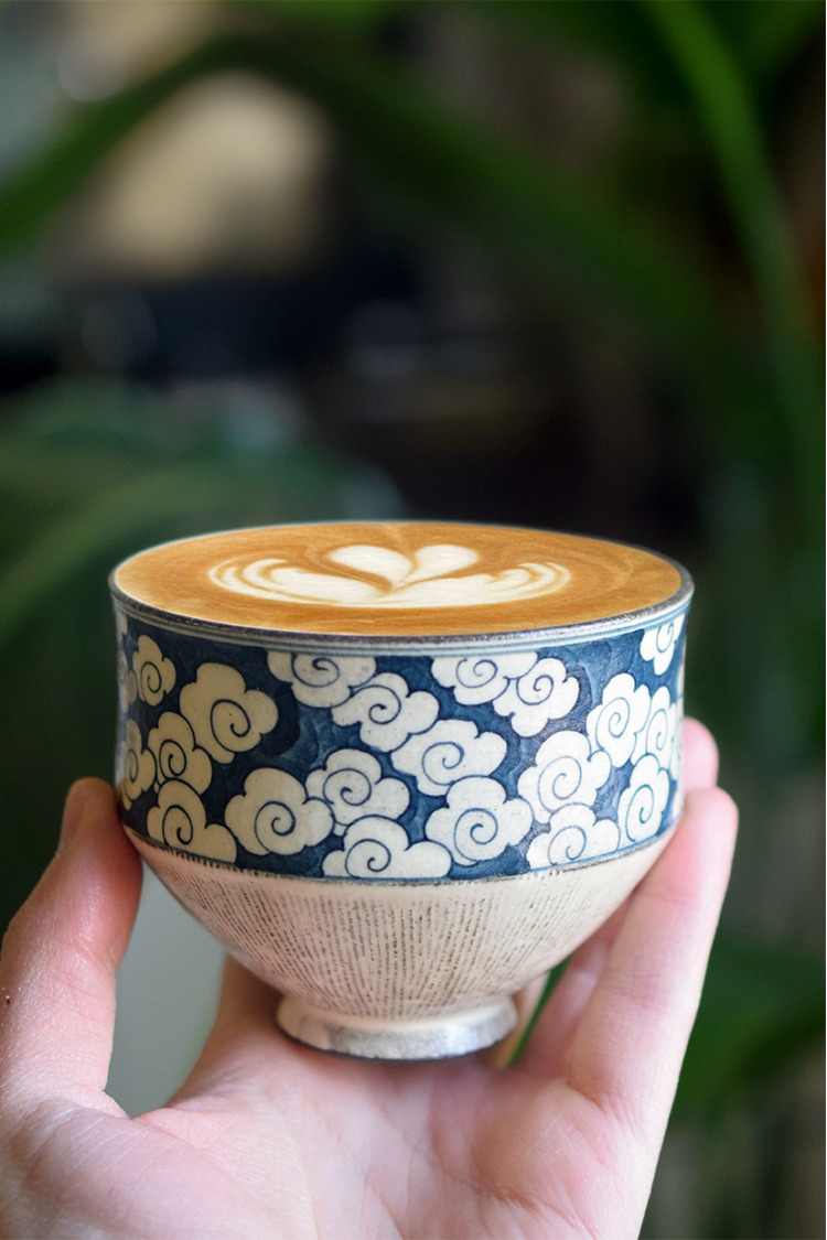 Hand holding handcrafted ceramic coffee cup with detailed underglaze cloud design and smooth artistic finish