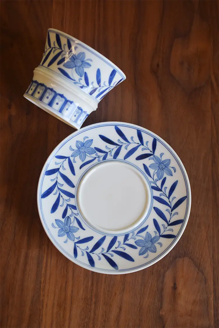 Custom blue and white ceramic cup and saucer display the intricate underglaze vine motif, blending elegance with traditional craftsmanship.
