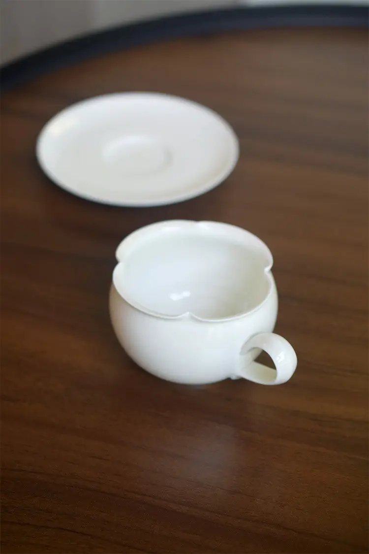 Pure white ceramic cup and saucer with floral edge design, showcasing minimalist elegance and craftsmanship.