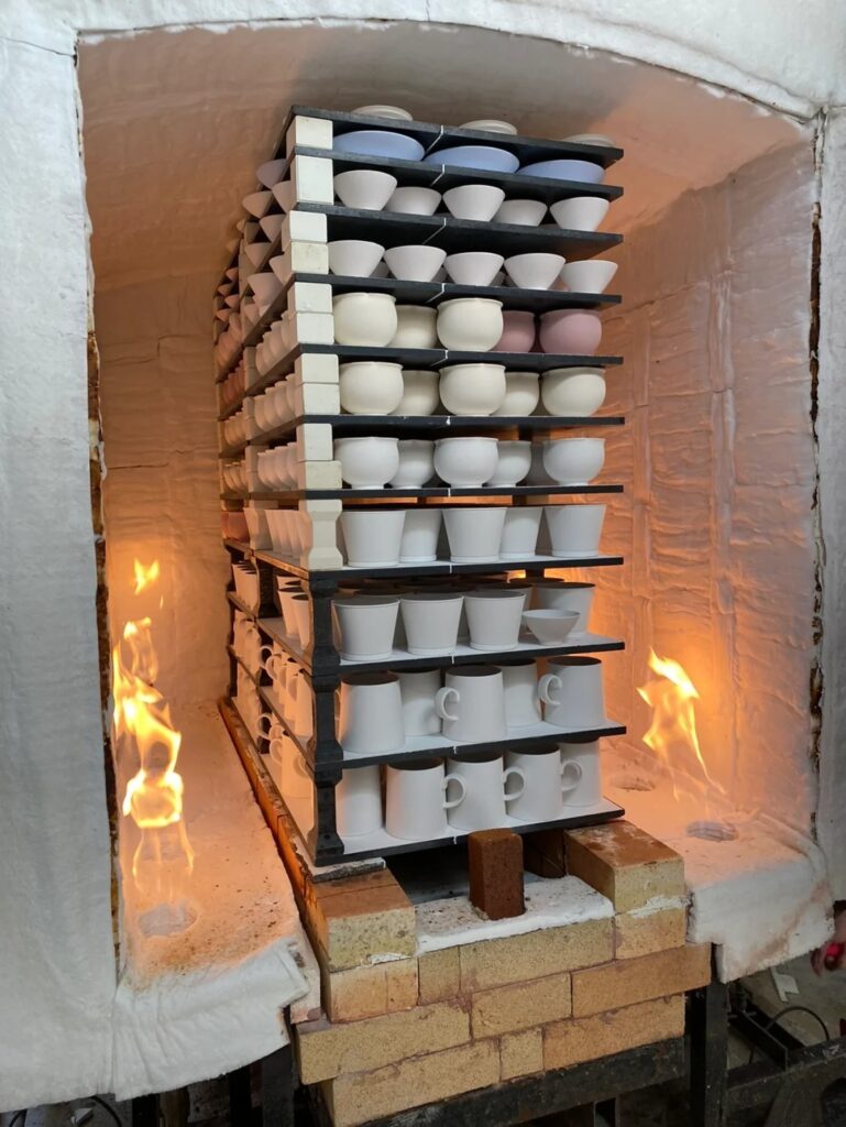 Placing hand-thrown ceramic cups into a kiln for high-temperature firing