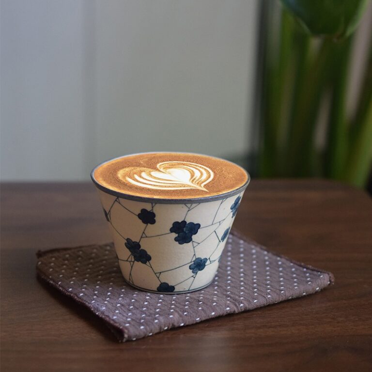 Handmade ceramic coffee cup with delicate artisan details, placed on a rustic wooden surface